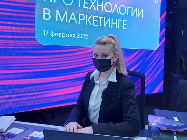 Девушка хостес в маске за стойкой регистрации